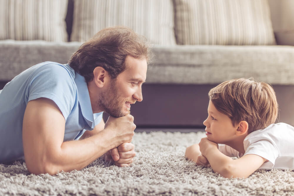 Side View of Handsome Father and His Cute Son Looking at Each Other and Smiling While Spending Time Together at Home