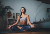 Young healthy beautiful woman in sports top and leggings practice, sitting on yoga mat with lotus attitude, meditating smile