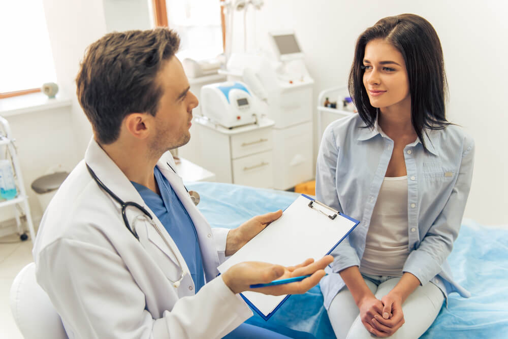 Handsome Doctor Is Talking With Young Female Patient and Making Notes While Sitting in His Office