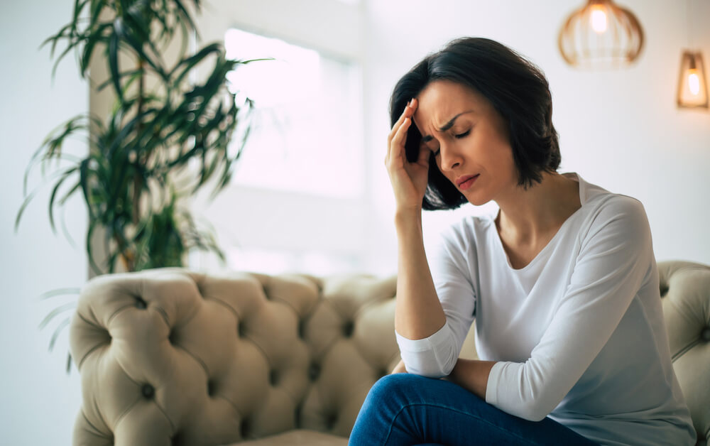 Close-up Photo of a Young Woman, Who Is Sitting on a Sofa With Her Eyes Closed, Touching Her Head While Suffering From a Migraine