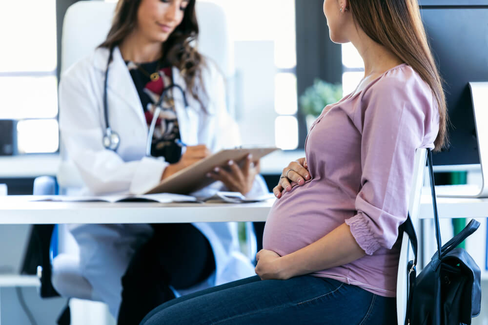 Shot of Pretty Young Woman Gynecologist Reviewing the Documents of Her Pregnant Patient in the Clinic