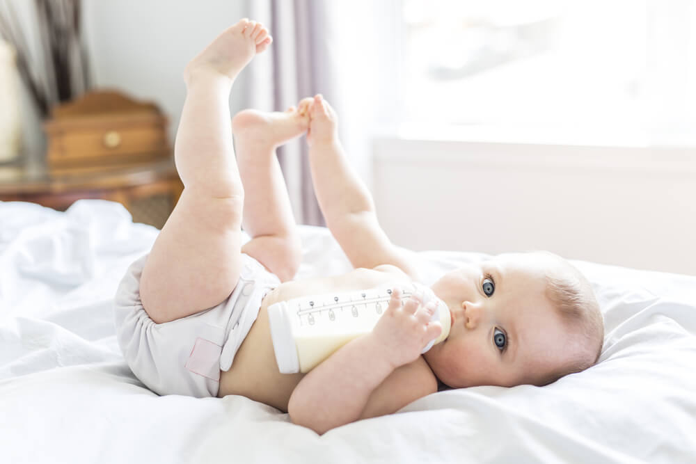 A Pretty Baby Girl Drinks Water From Bottle Lying on Bed