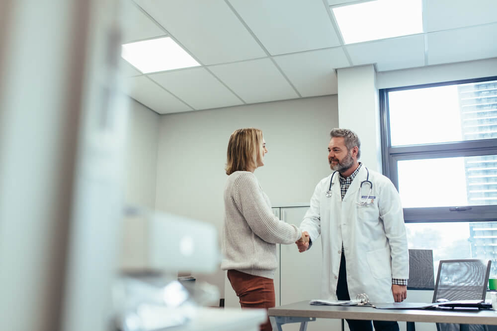 Male Physician Shaking Hands With Patient in Clinic.