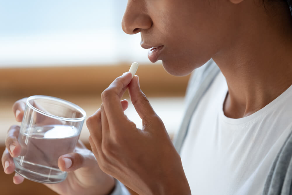 Close Up of Young Woman Hold Glass of Water and White Pills at Her Mouth