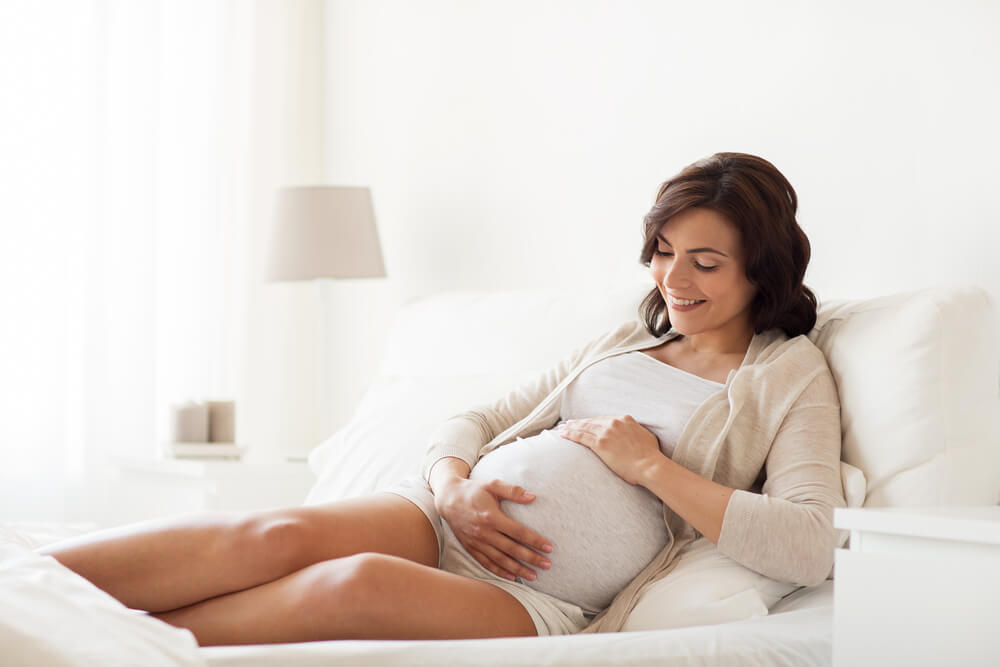 Happy Pregnant Woman Lying on Bed and Touching Her Belly