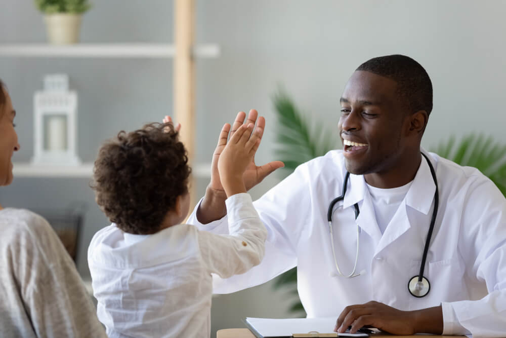 Smiling African American Pediatrician Doctor Giving High Five to Little Boy Patient