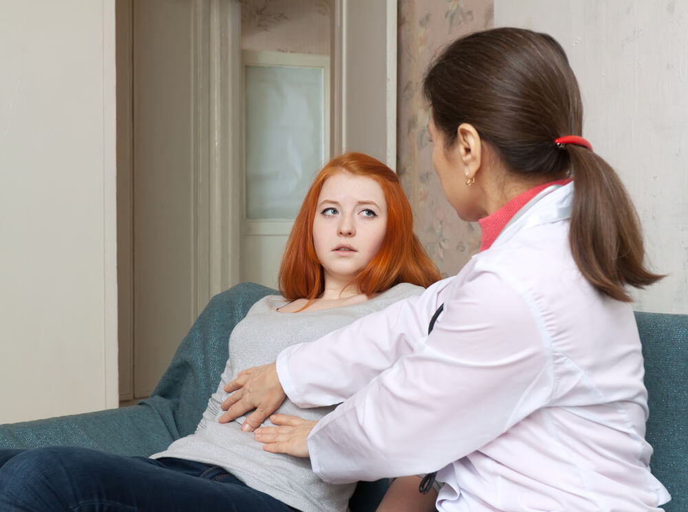 Mature Doctor Touches Belly of Teenager Patient in Interior