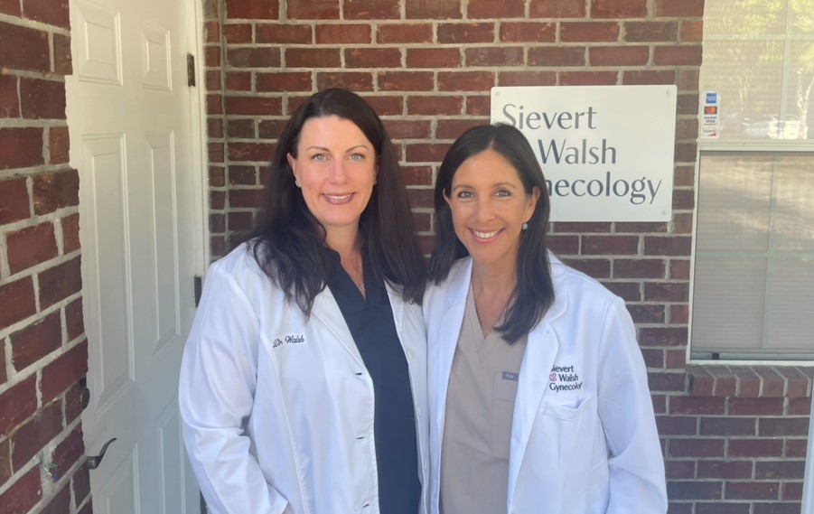 Two female doctors standing together outside in front of their office