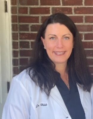 Woman in doctor's coat standing outside in front of brick wall